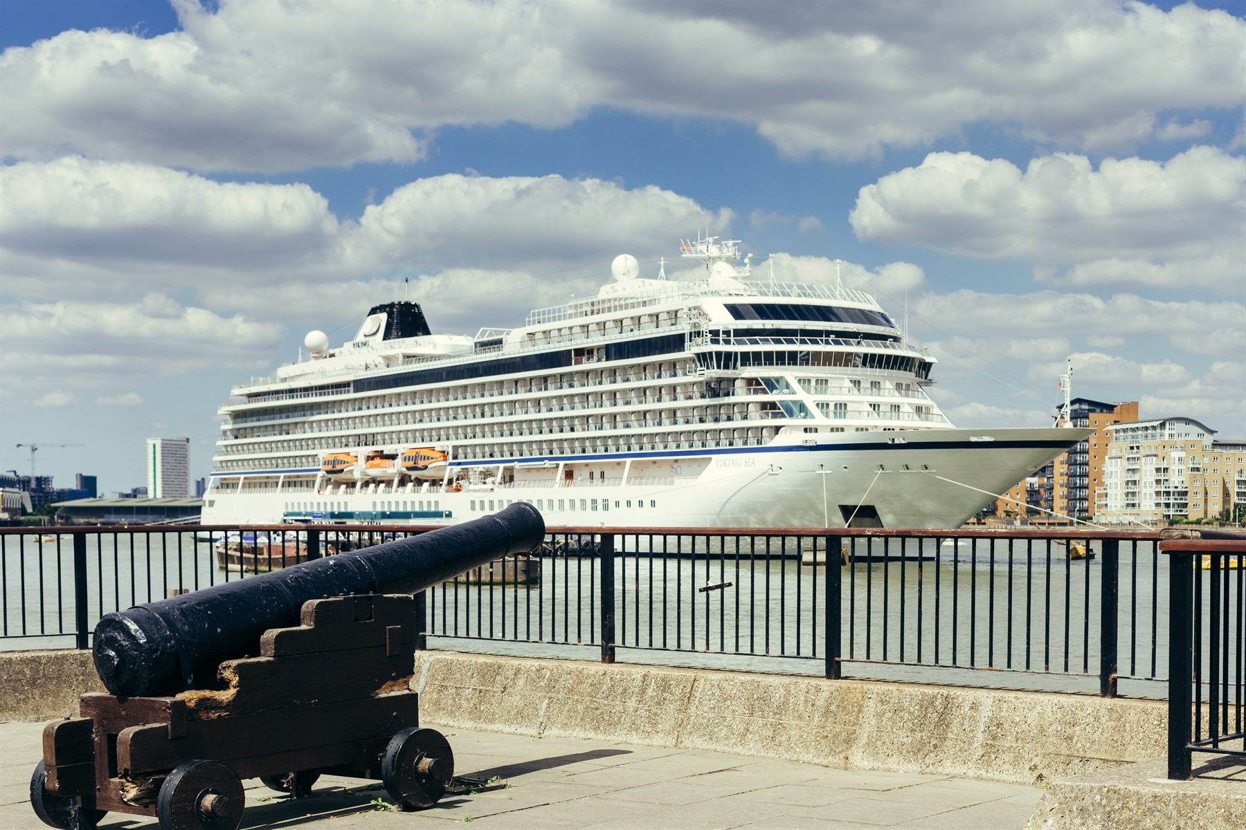 A Viking ocean ship moored on a river, seen past an old cannon on the embankment