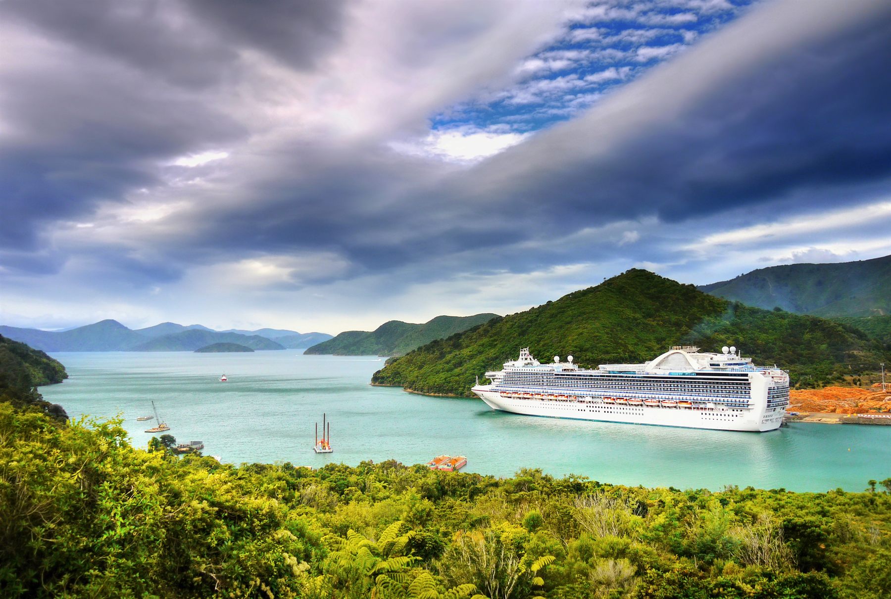 A cruise ship anchored in a turquoise bay ringed by green, forested hills